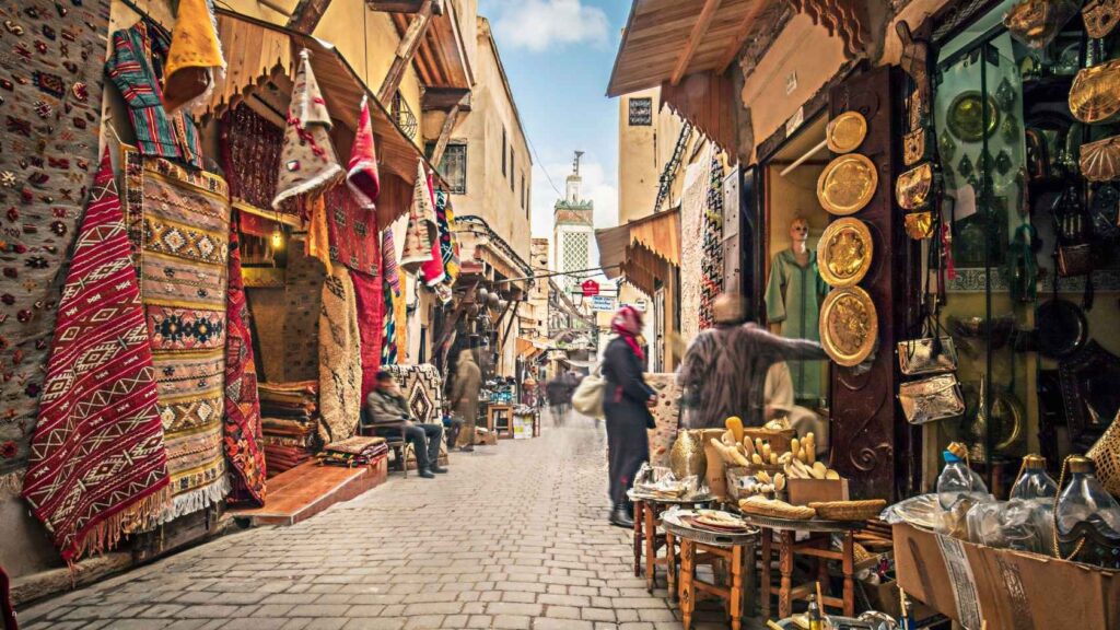Busy street in the Fes medina with traditional souks selling carpets, brassware, and Moroccan handicrafts